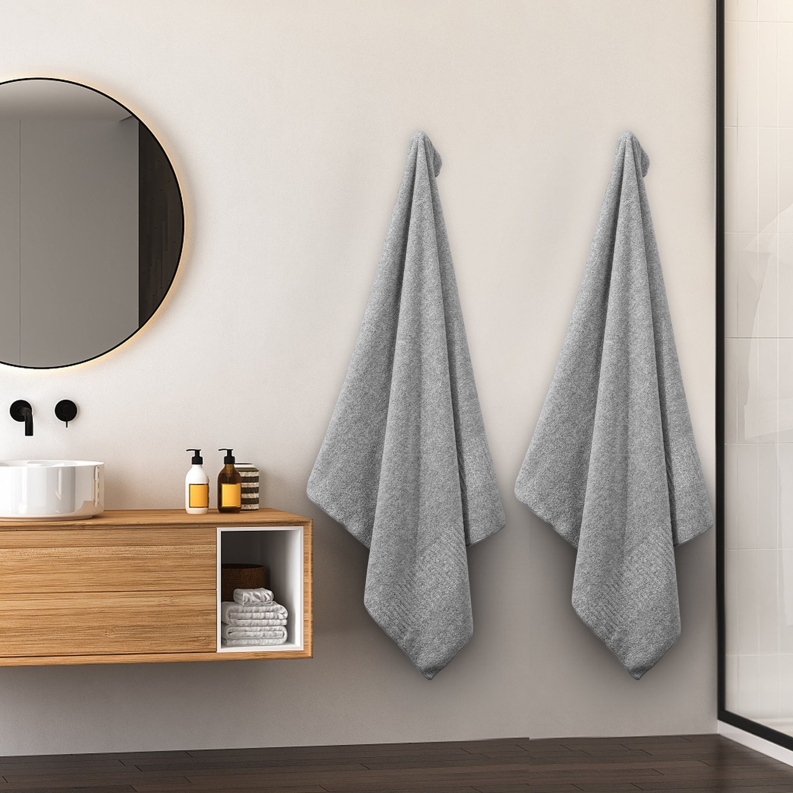 Seisso Gray bath towels hanging on a wall in a modern bathroom with a wooden cabinet and round mirror.